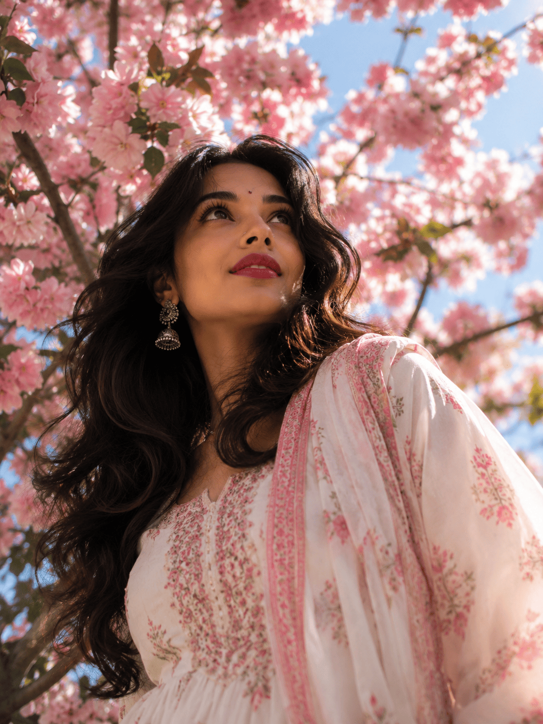 Cherry blossom low-angle portrait example Tech Upkar Low Angle AI Photo prompt example showing a woman looking upward beneath blooming pink cherry blossoms